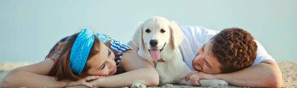 White dog laying between male and female on the beach